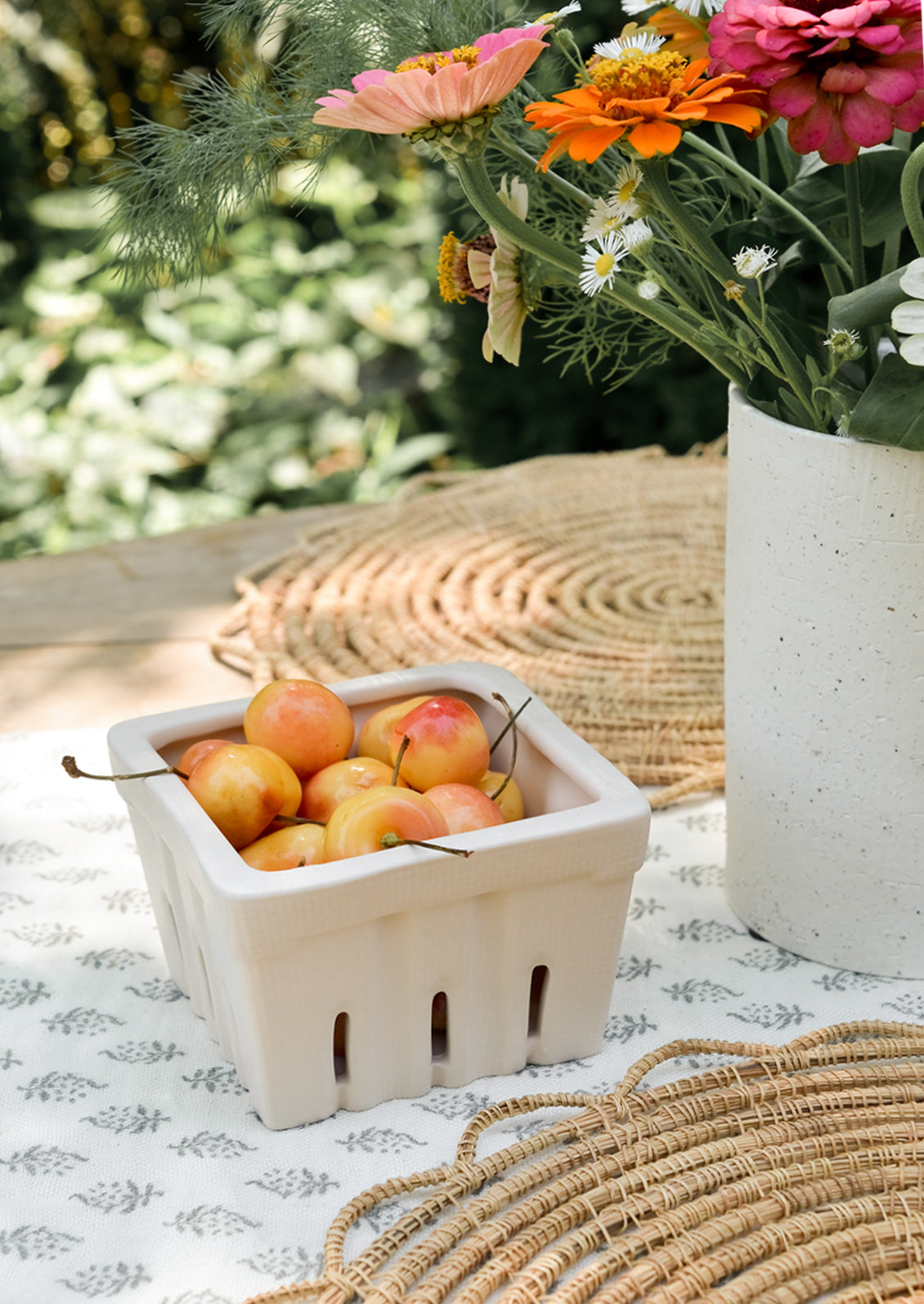 A ceramic berry basket on a table, filled with cherries.