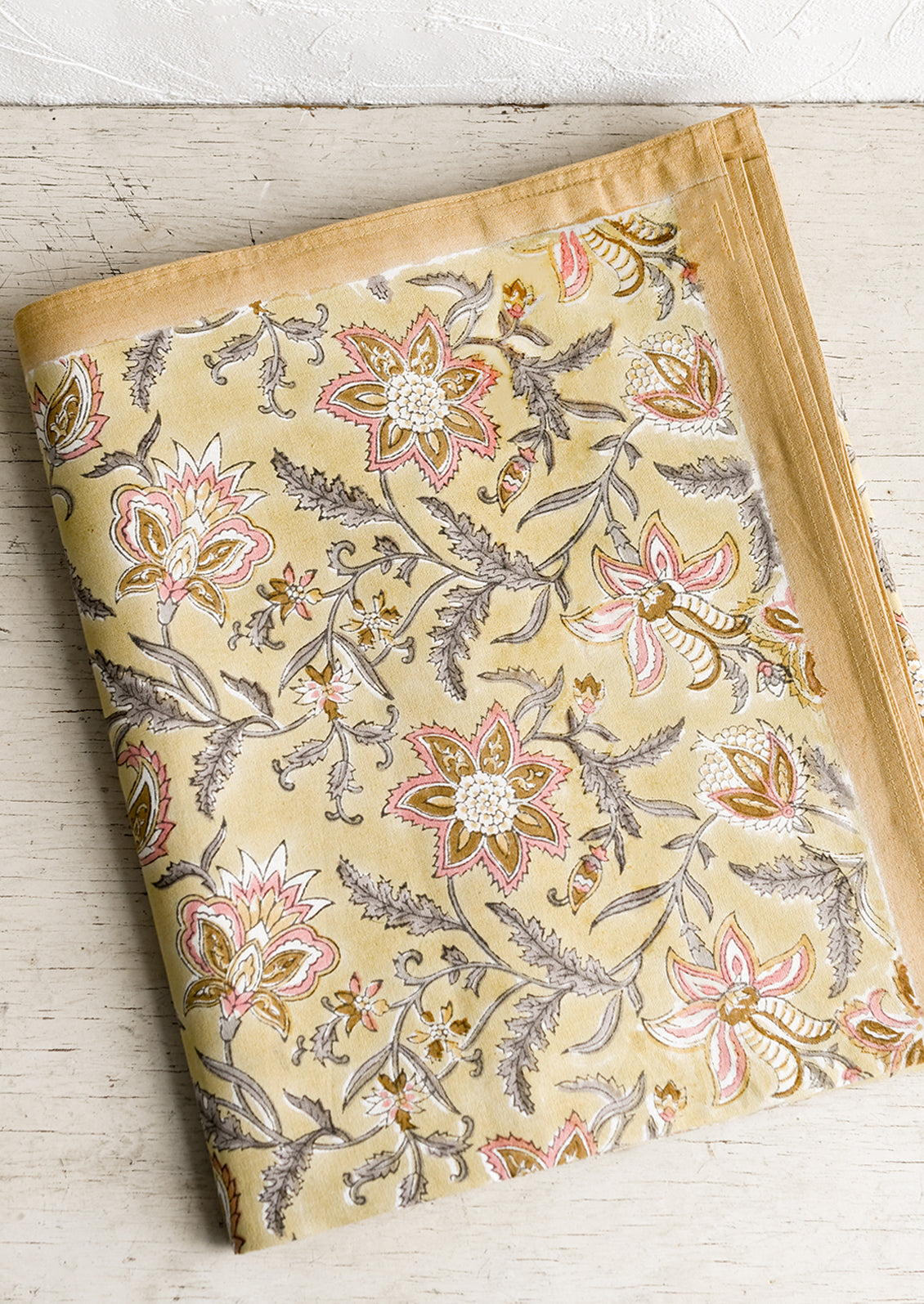 A pale yellow tablecloth with floral print in grey and pink.
