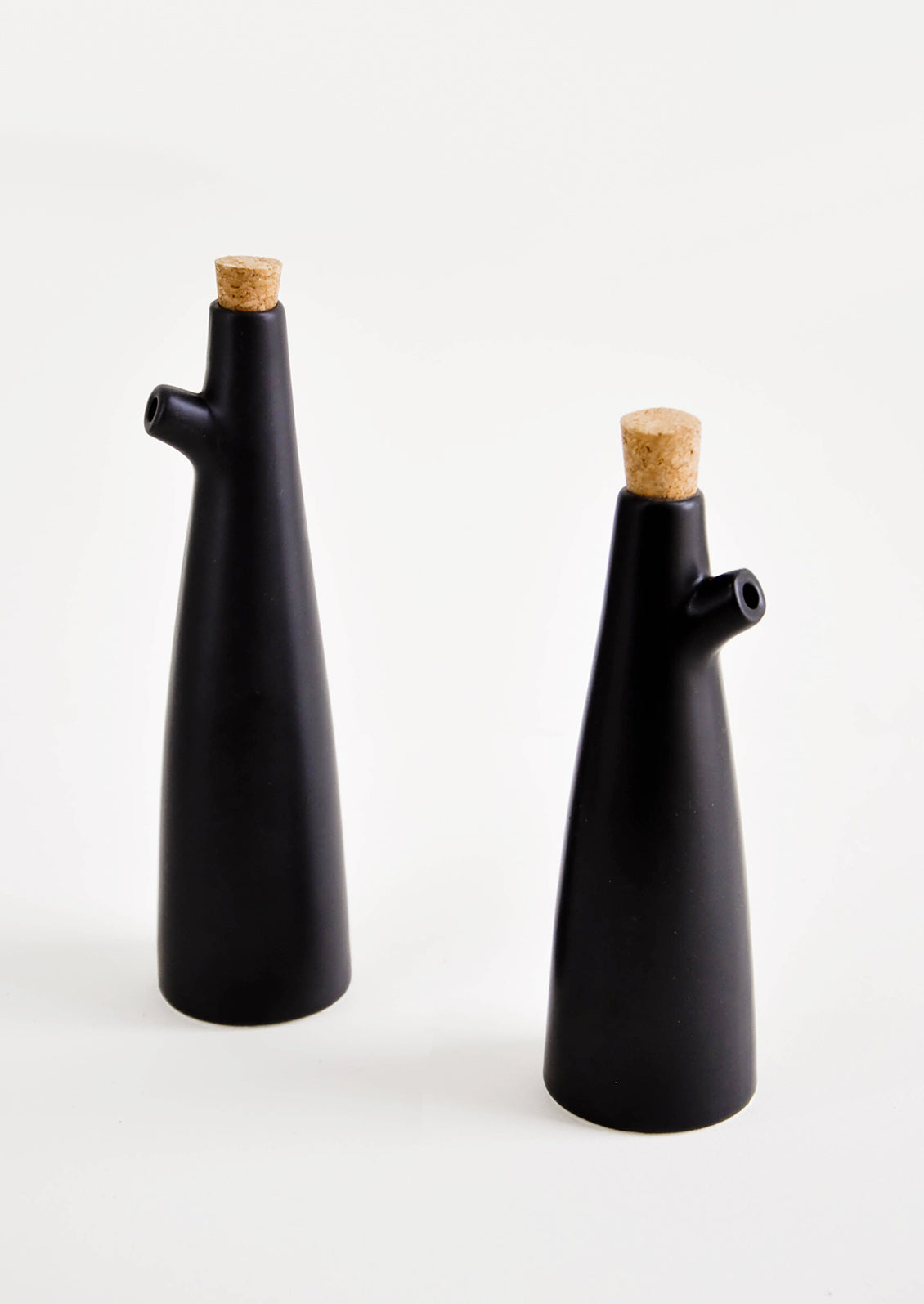 Ceramic cruets for oil & vinegar, one taller than the other. Matte black glaze, cork stopper as lid.