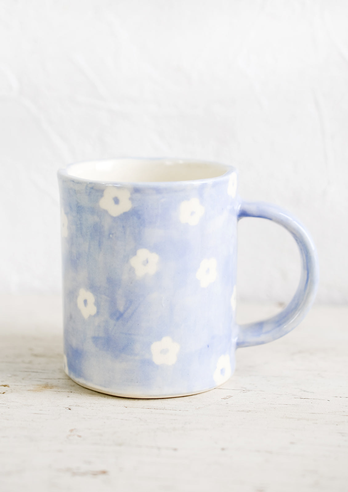 A handmade ceramic mug with periwinkle background and hand-painted white flowers.