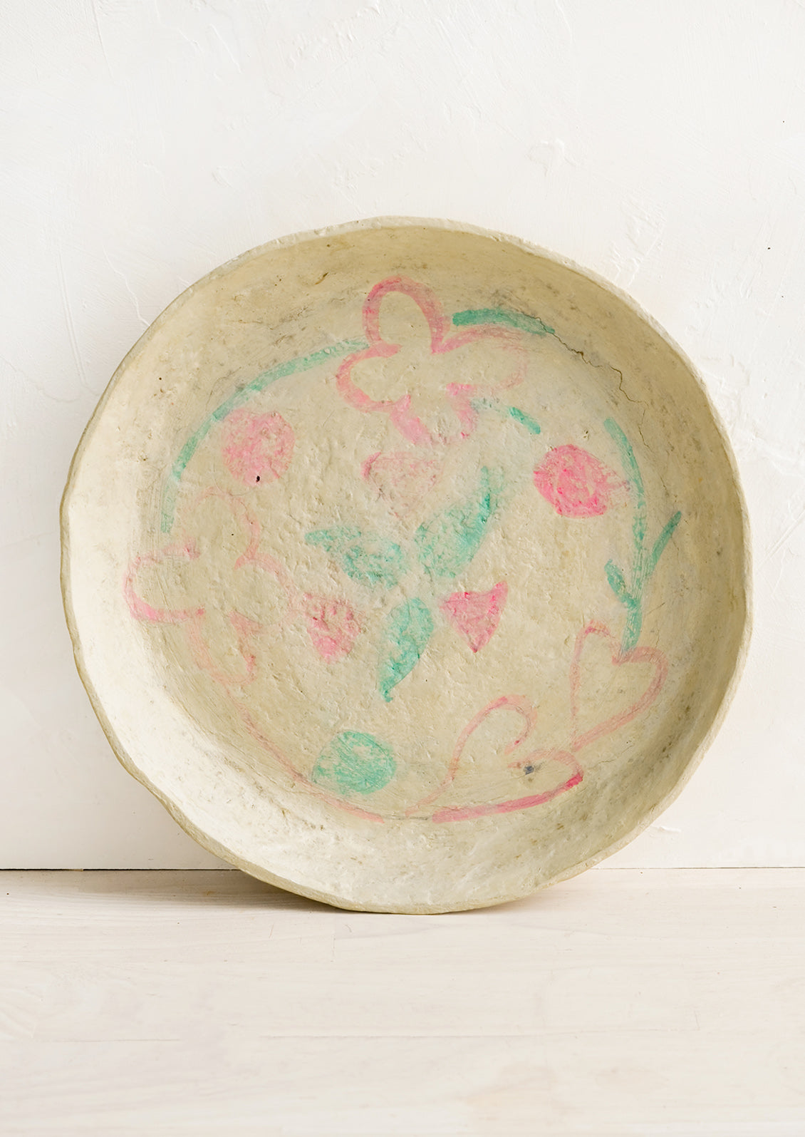 A round paper mache tray with faded pink and green design.