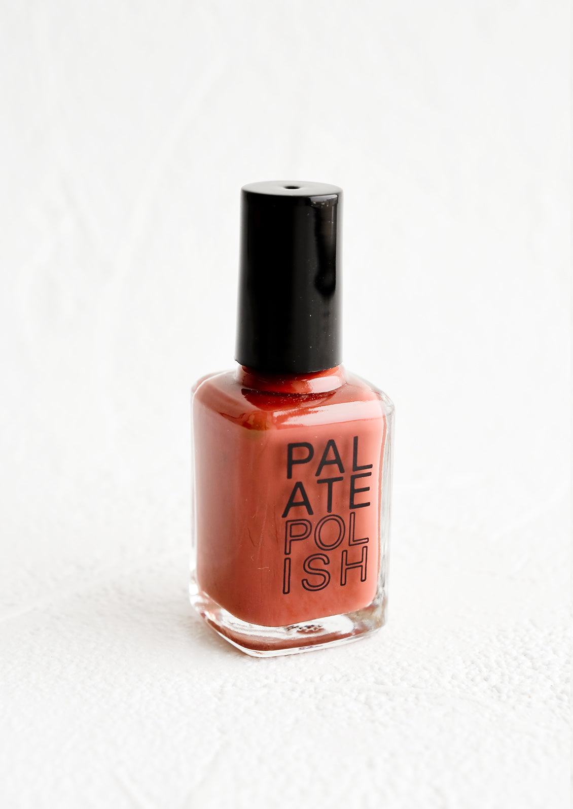 A bottle of nail polish in desaturated cherry red.