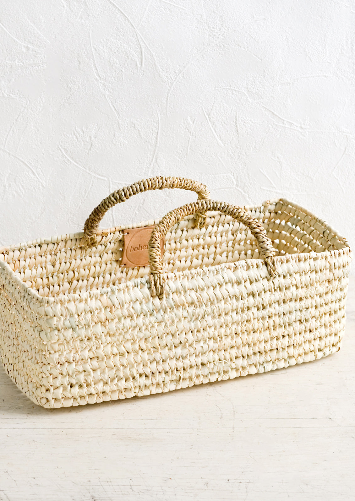 A skinny and narrow square storage basket with handles, made from natural dried palm.
