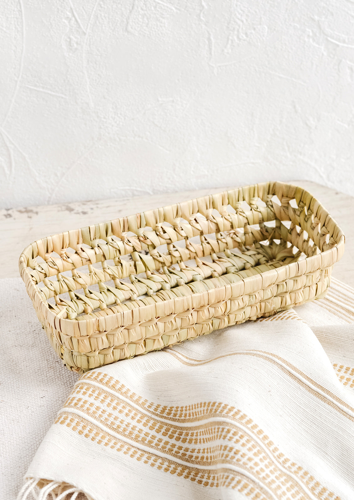 A shallow, narrow storage basket made from dried palm leaf.