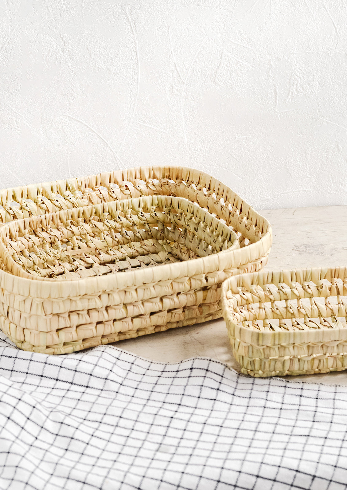 A collection of shallow nesting baskets made from palm leaf.