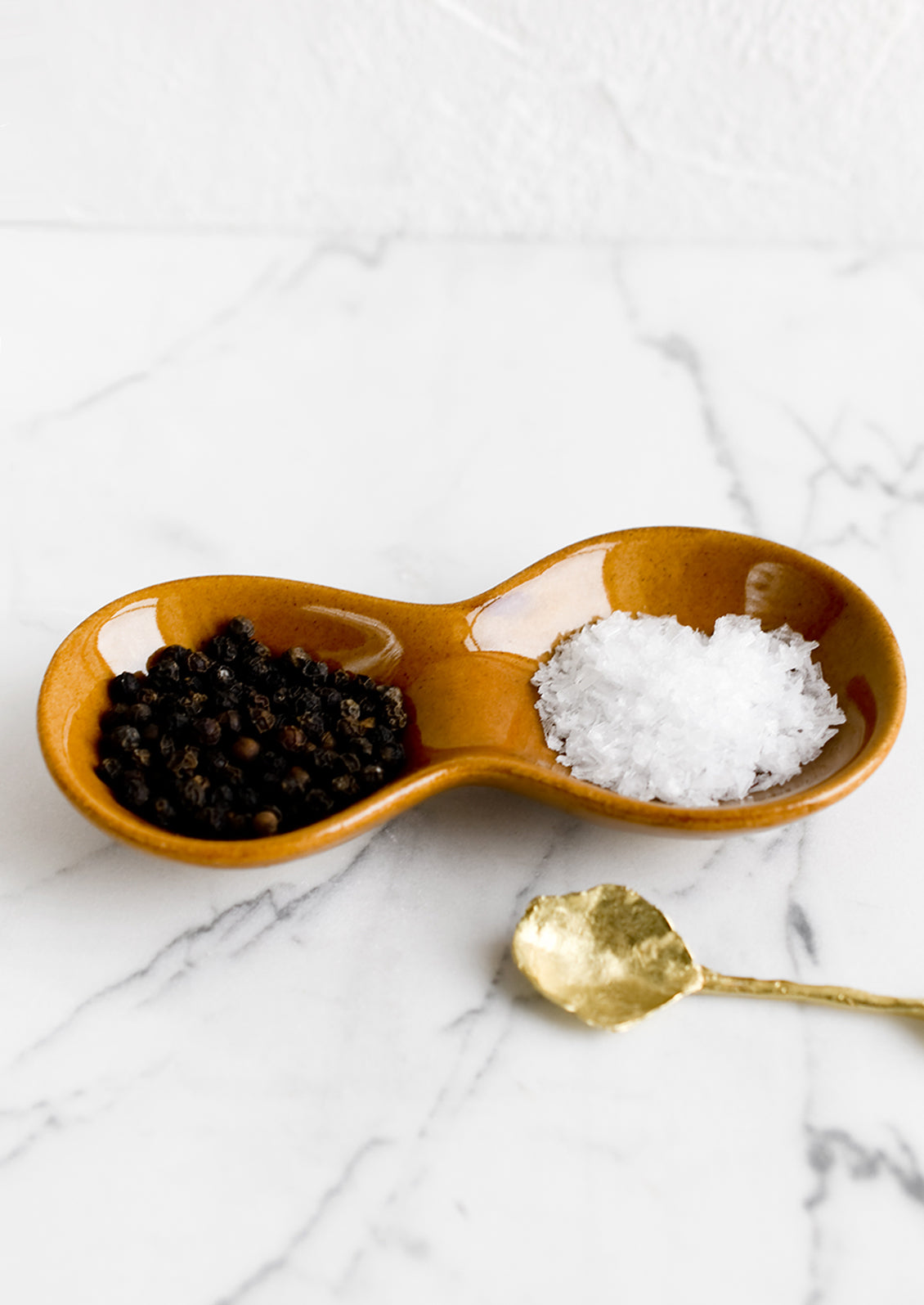 A glossy caramel colored ceramic dish holding salt and pepper.