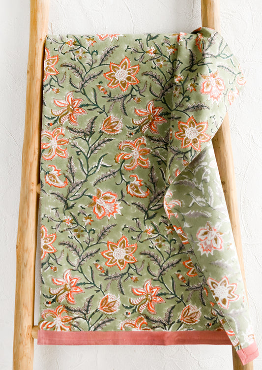 A tea towel with sage green background and orange and pink floral print.