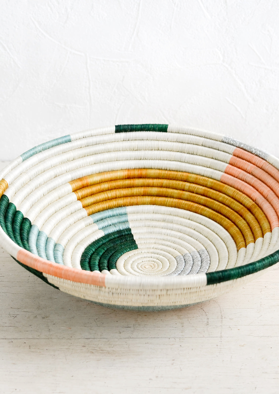 A round bowl made from woven sweetgrass in white, multiple pastels and silver.