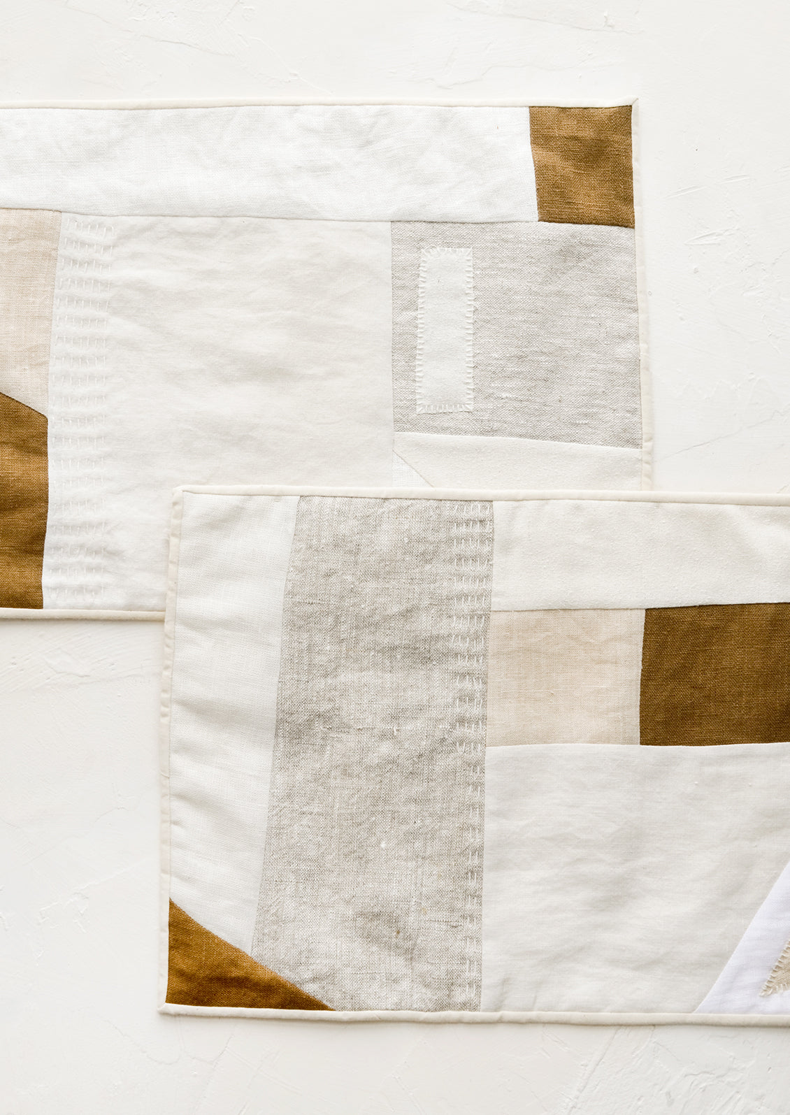 A pair of rectangular placemats with patchwork design in natural shades.