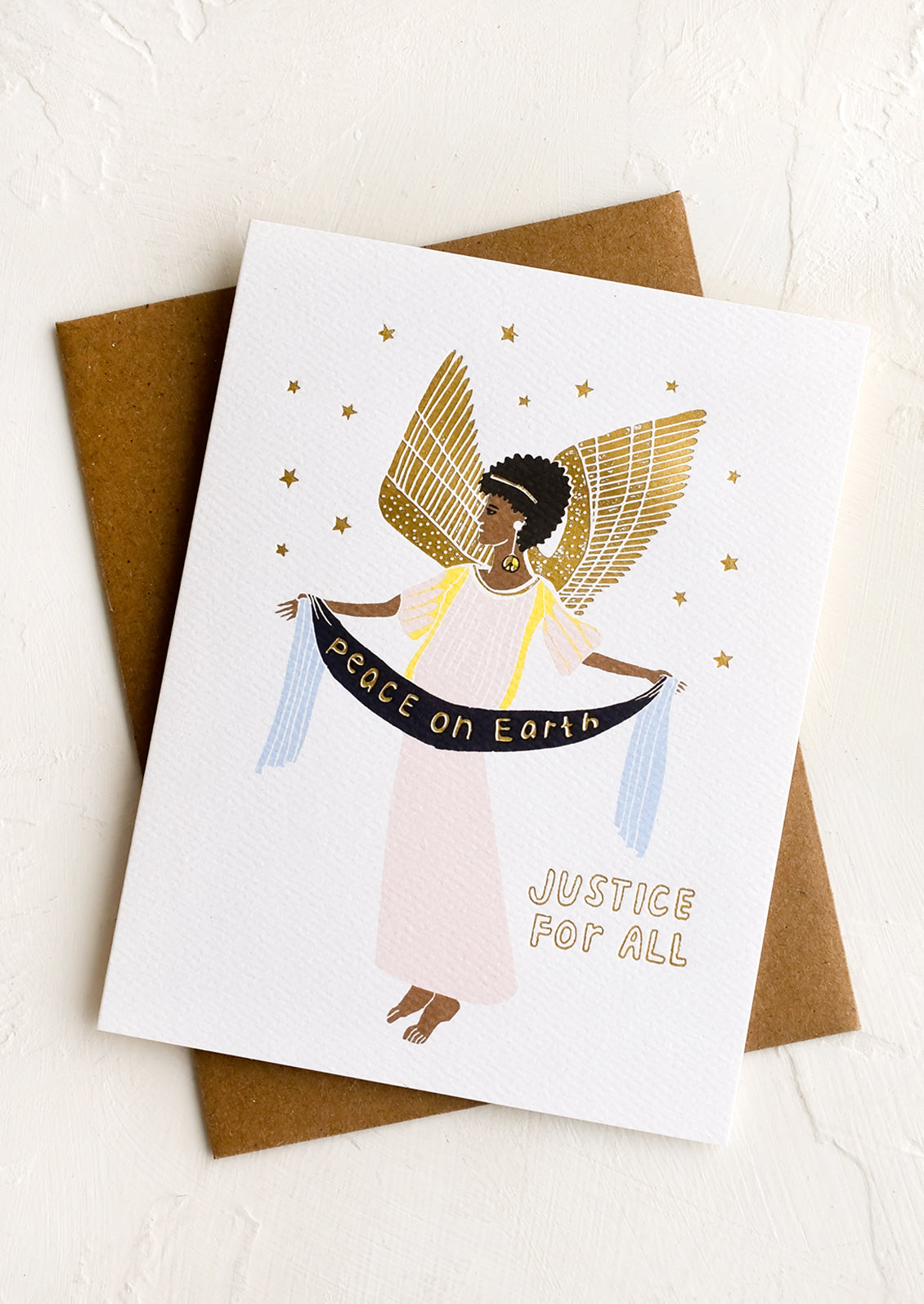 A greeting card with image of woman as an angel holding a flag reading "peace on earth justice for all".