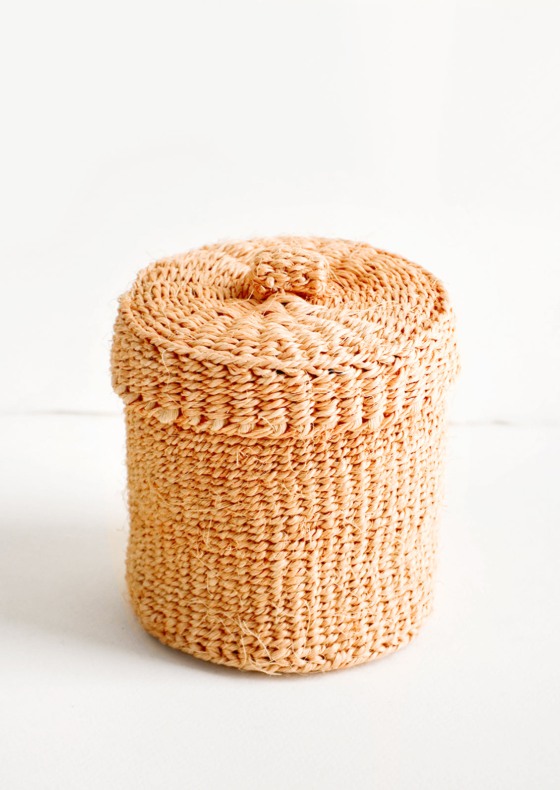 Small, round woven basket with matching lid made from peach-colored sisal