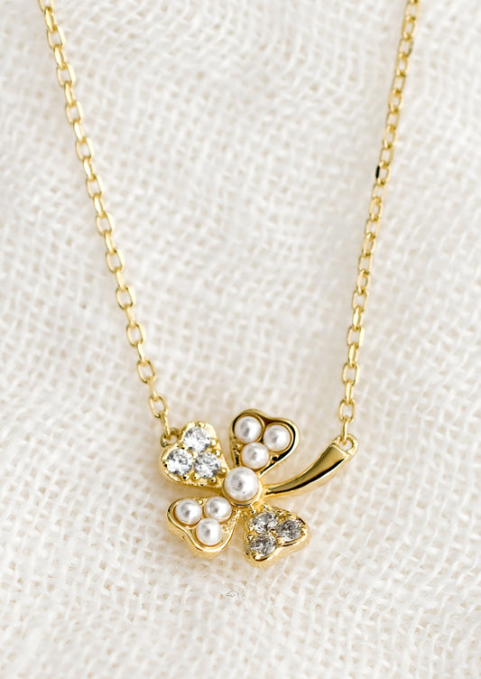 A gold necklace with clover pendant detailed with clear crystals and pearls.