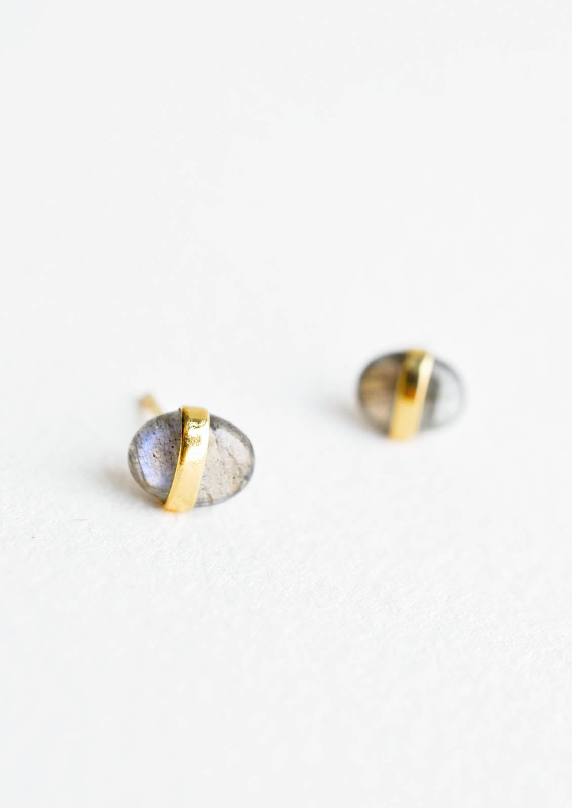 Oval-shaped, pebble-like stud earrings in iridescent labradorite with golden band wrapped around middle.