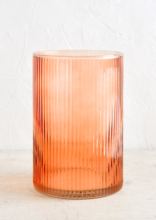 A fluted glass hurricane vase in peach color.