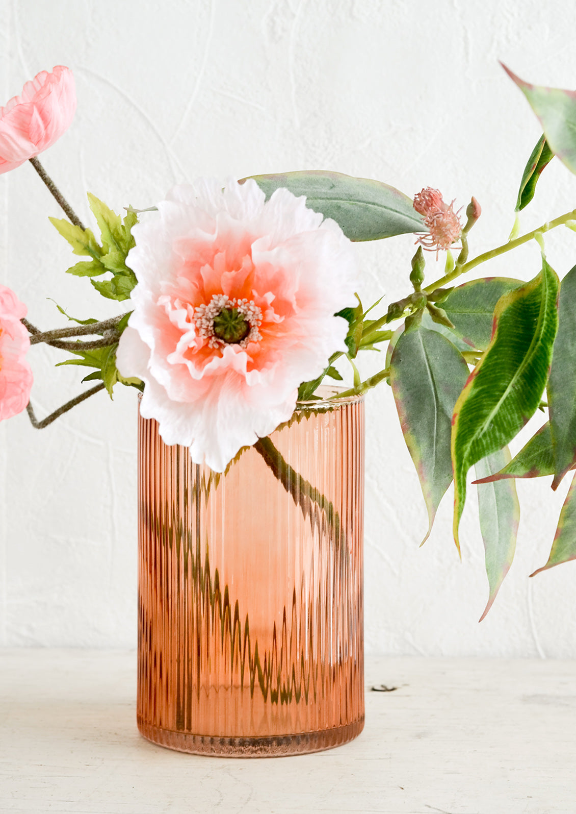 A fluted peach glass vase with pink and green flowers.
