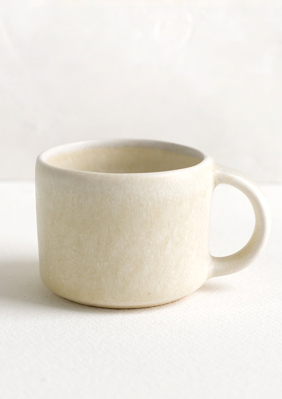 A ceramic espresso mug with handle in neutral ivory glaze.