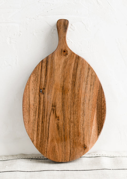 An oval shaped paddle-style cutting board in acacia wood.