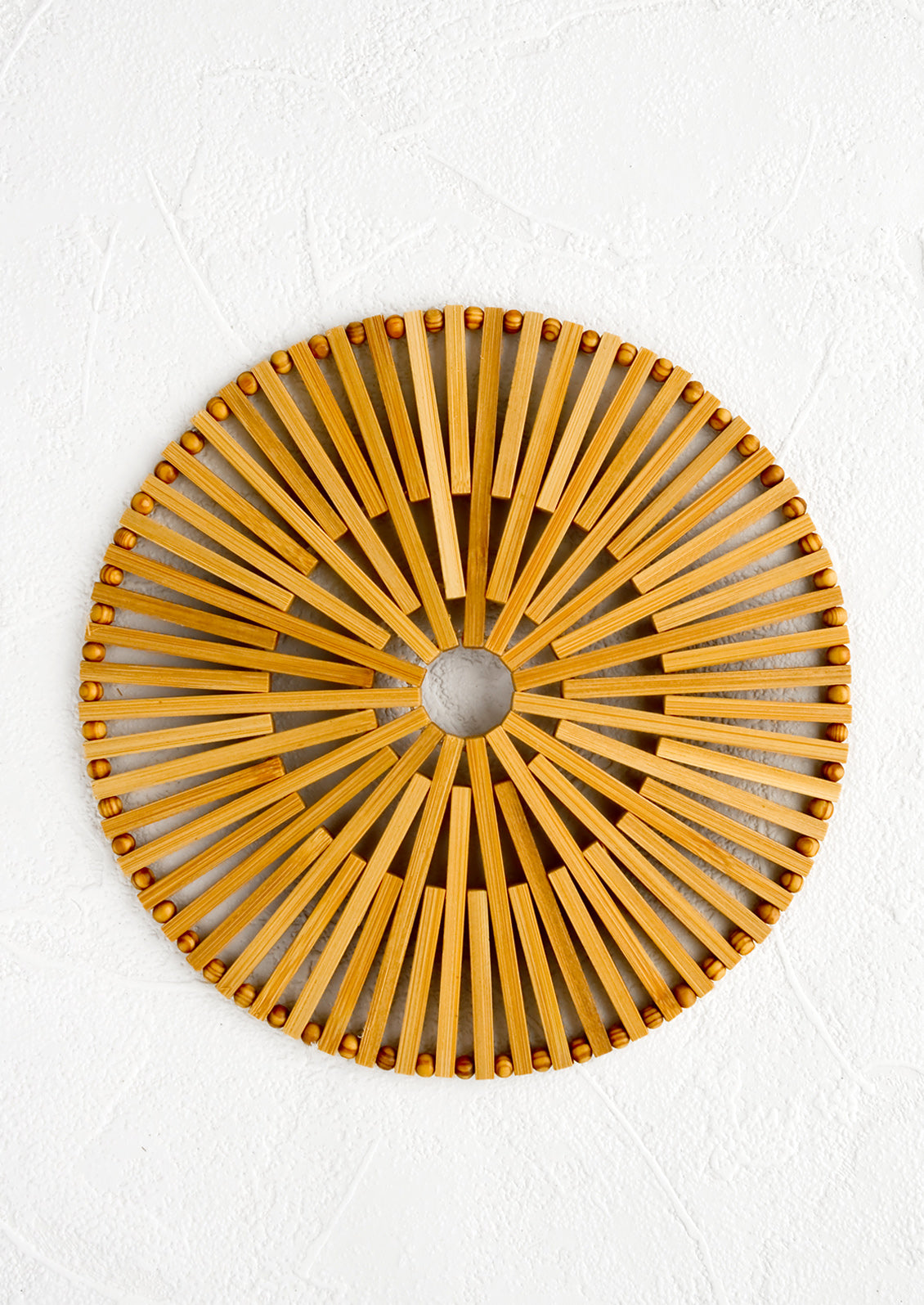 A round bamboo trivet with circular "sun" design.