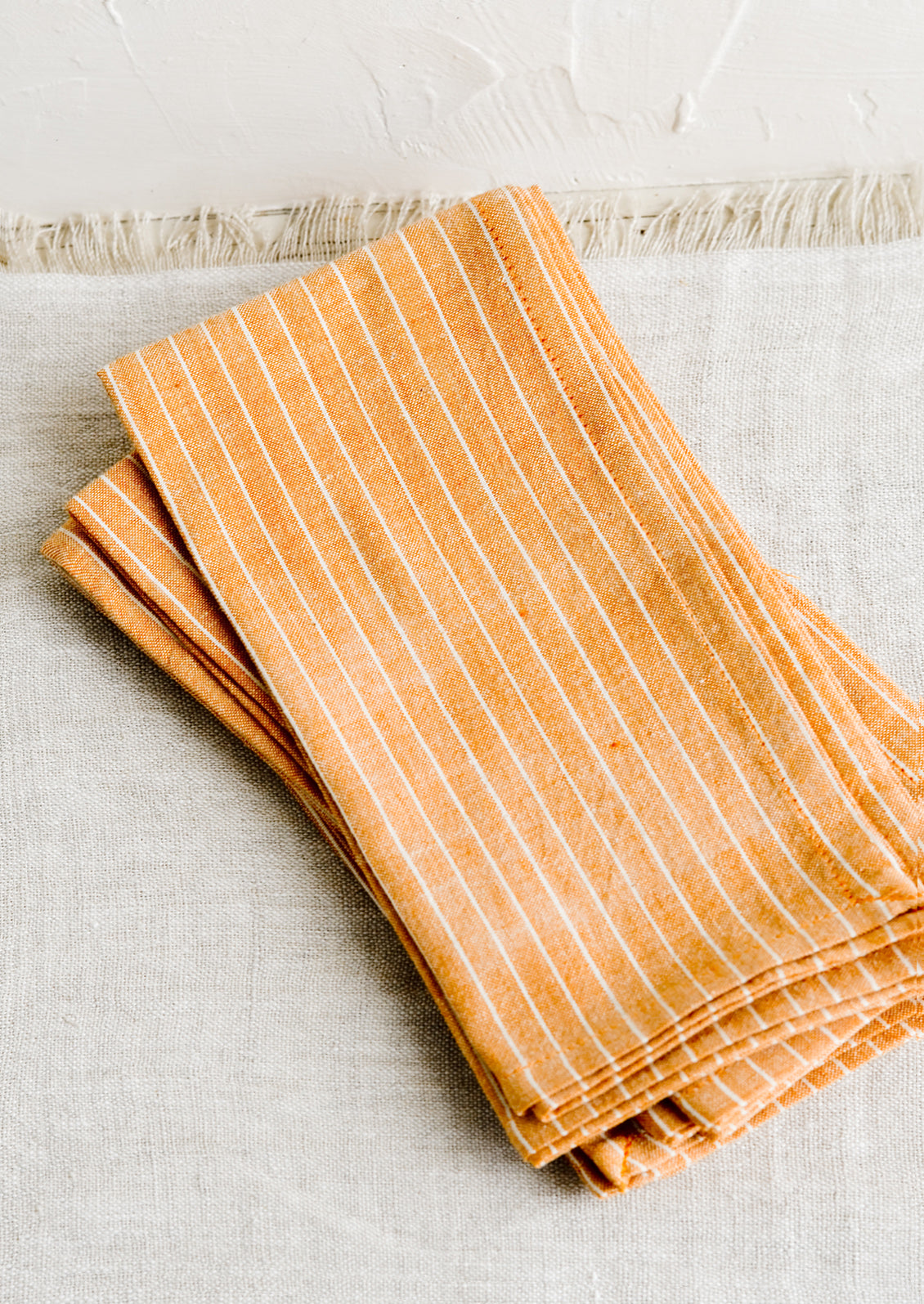 Folded fabric napkins in a pile featuring orange and white pinstripe pattern.
