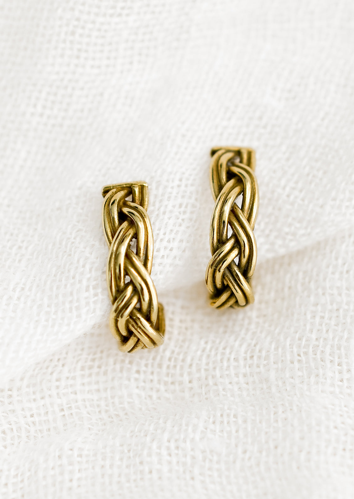 A pair of braided brass earrings that curve at bottom.