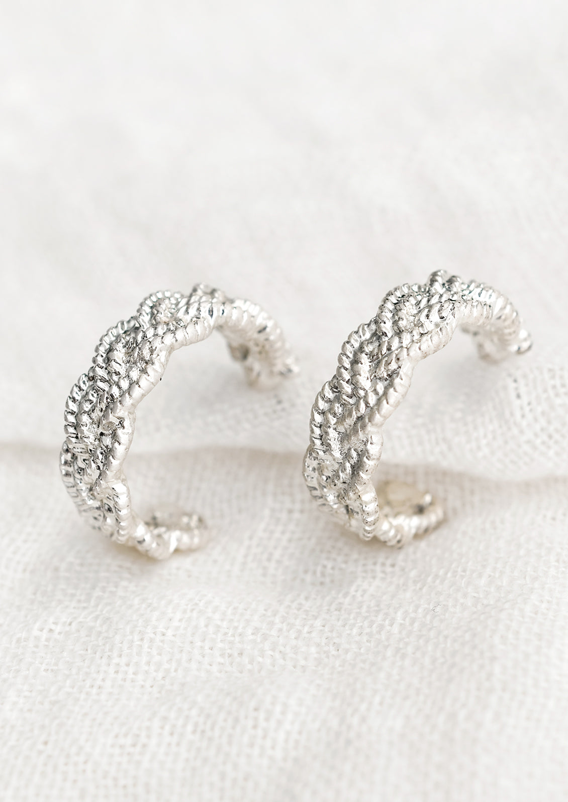 A pair of silver-tone hoop earrings with braided texture.