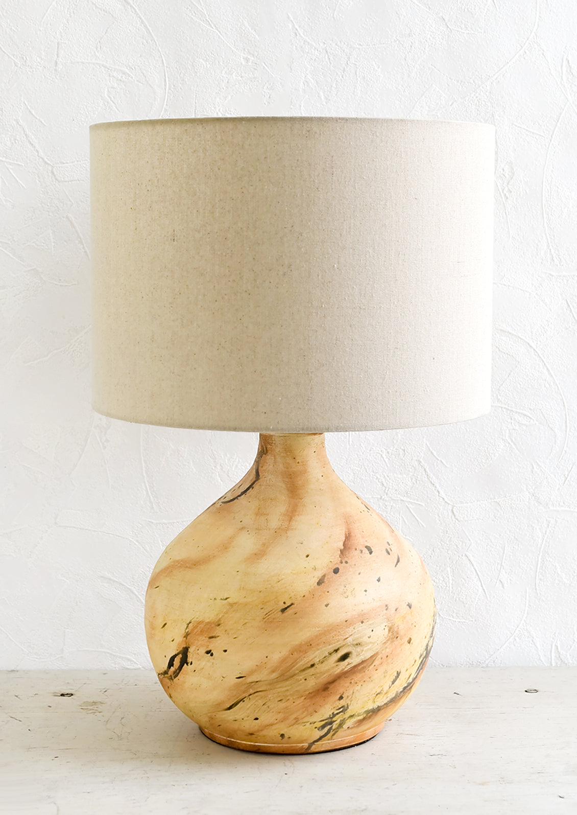 A table lamp with round ceramic base with paint splatter effect and round natural linen shade.