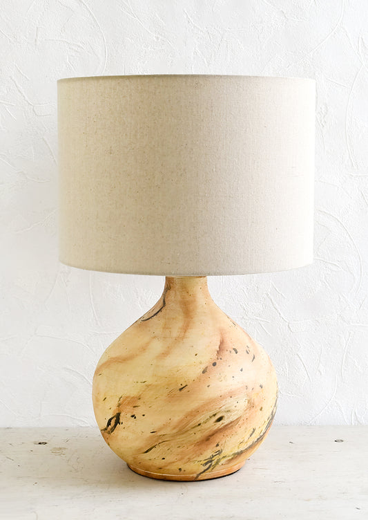 A table lamp with round ceramic base with paint splatter effect and round natural linen shade.