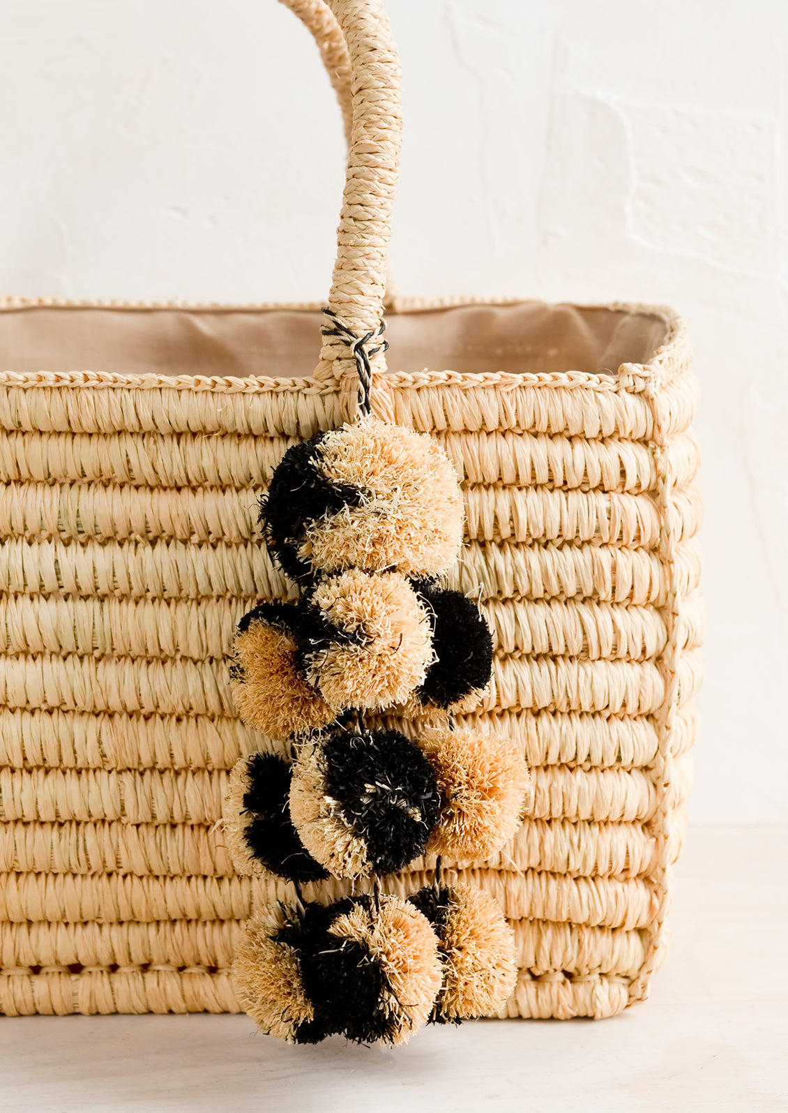 Pom pom detail on a raffia tote bag.