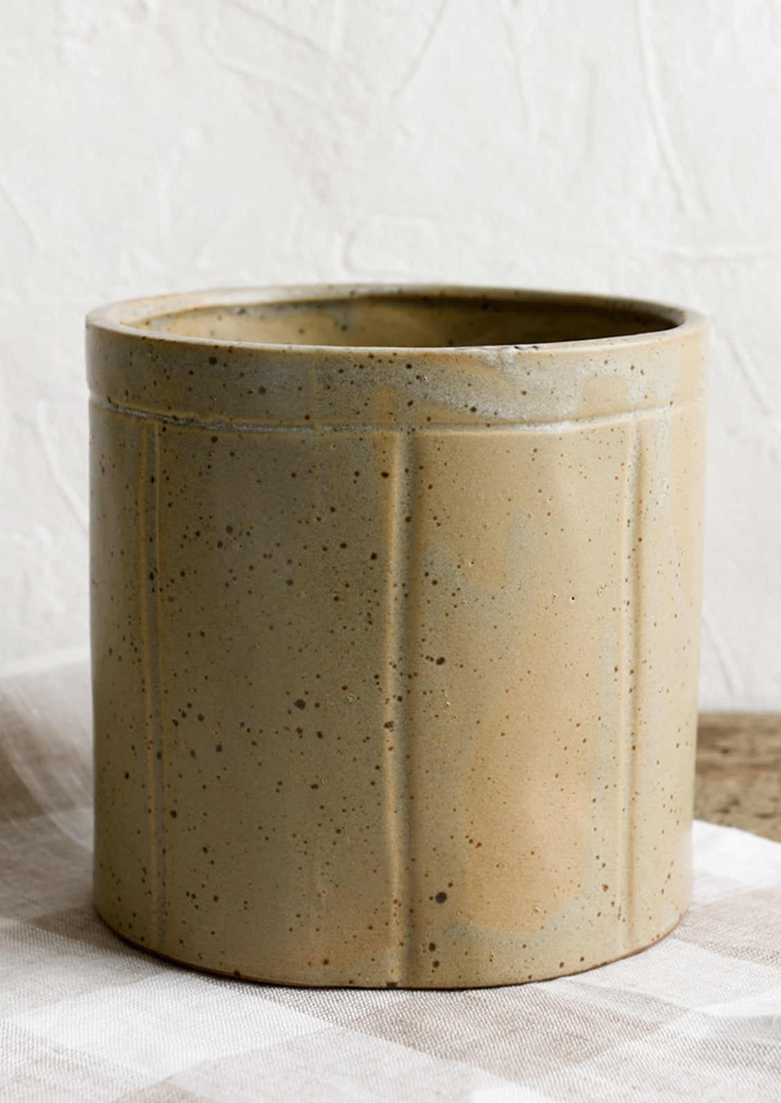 A round utensil crock in speckled tan ceramic with vertical line detail.