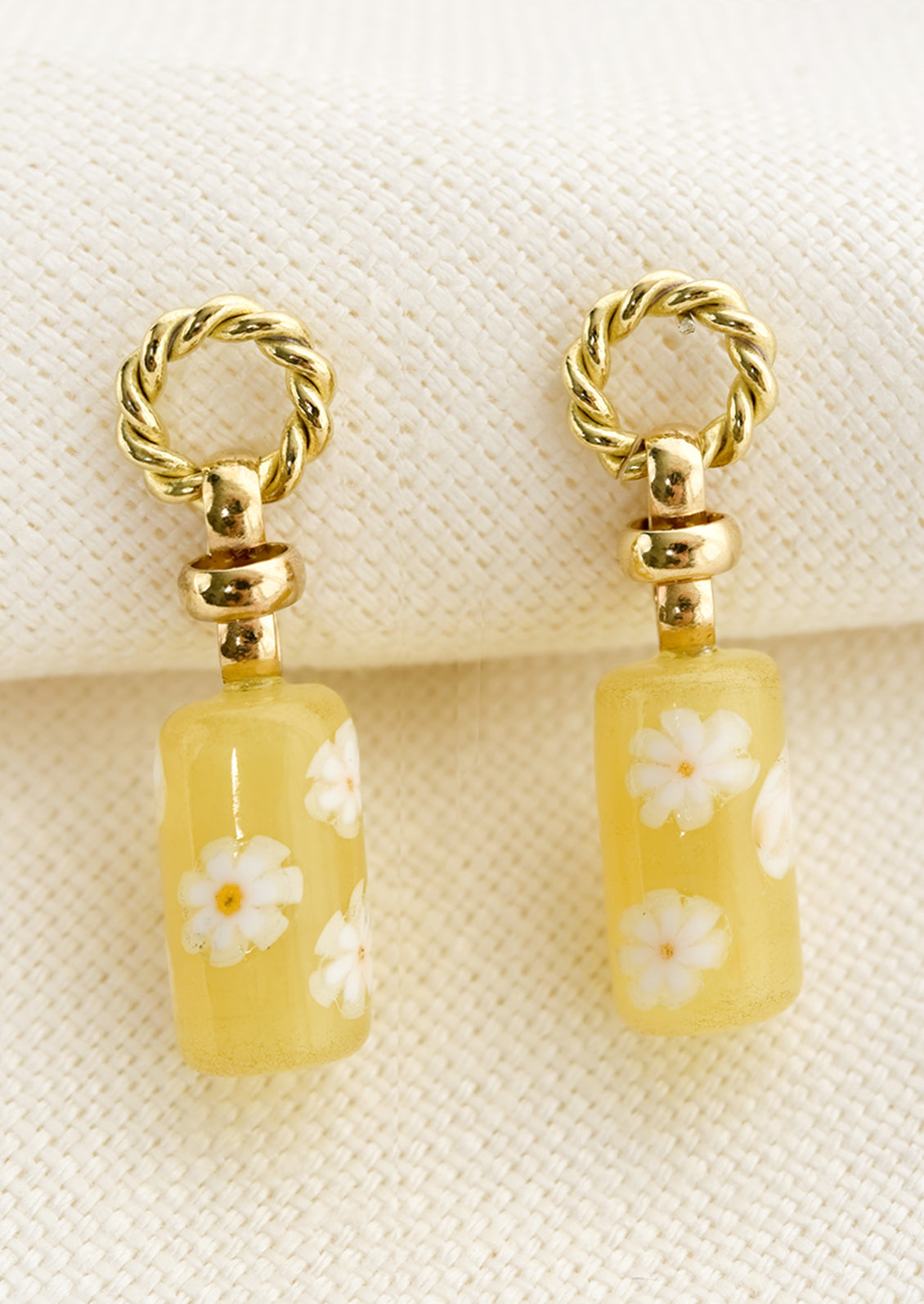 A pair of earrings with circular braided brass post and yellow floral glass bead.