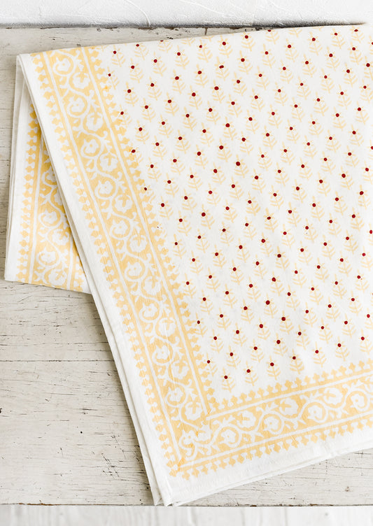 A cotton tablecloth in yellow and red floral block print motif.