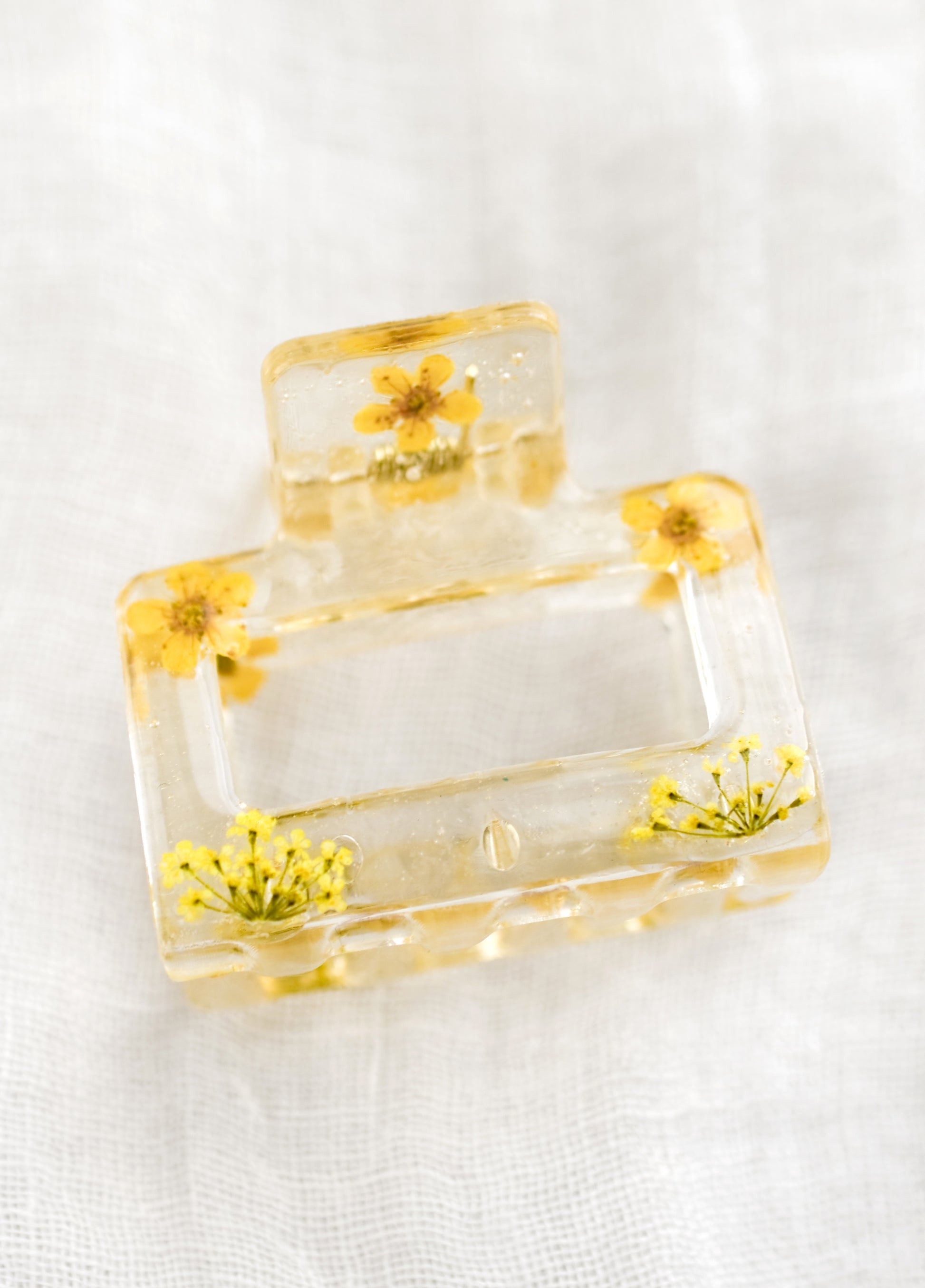 A square hair claw in clear resin with yellow dried flowers.