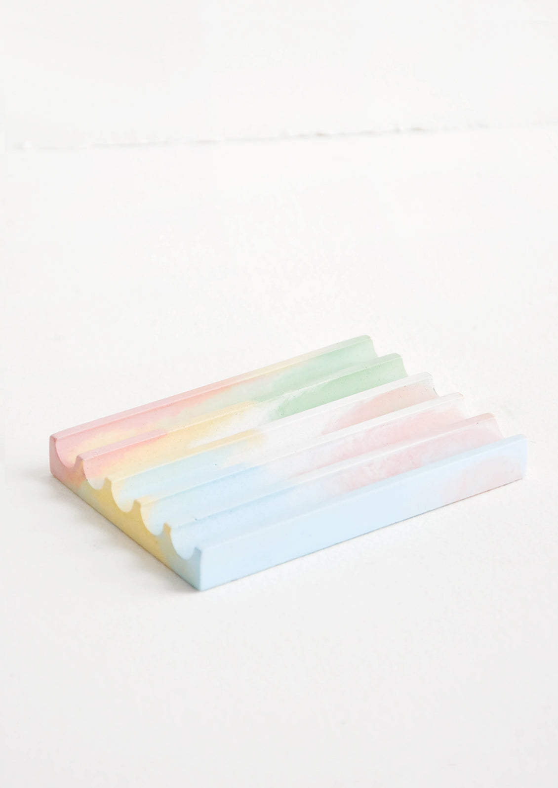 A marbled pink, yellow, blue, and green smooth concrete soap dish with troughs and ridges.