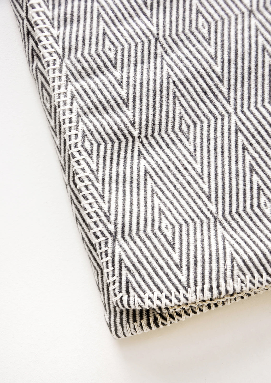 Cotton blanket with allover geometric diamond pattern in black and white, with whipstitched trim