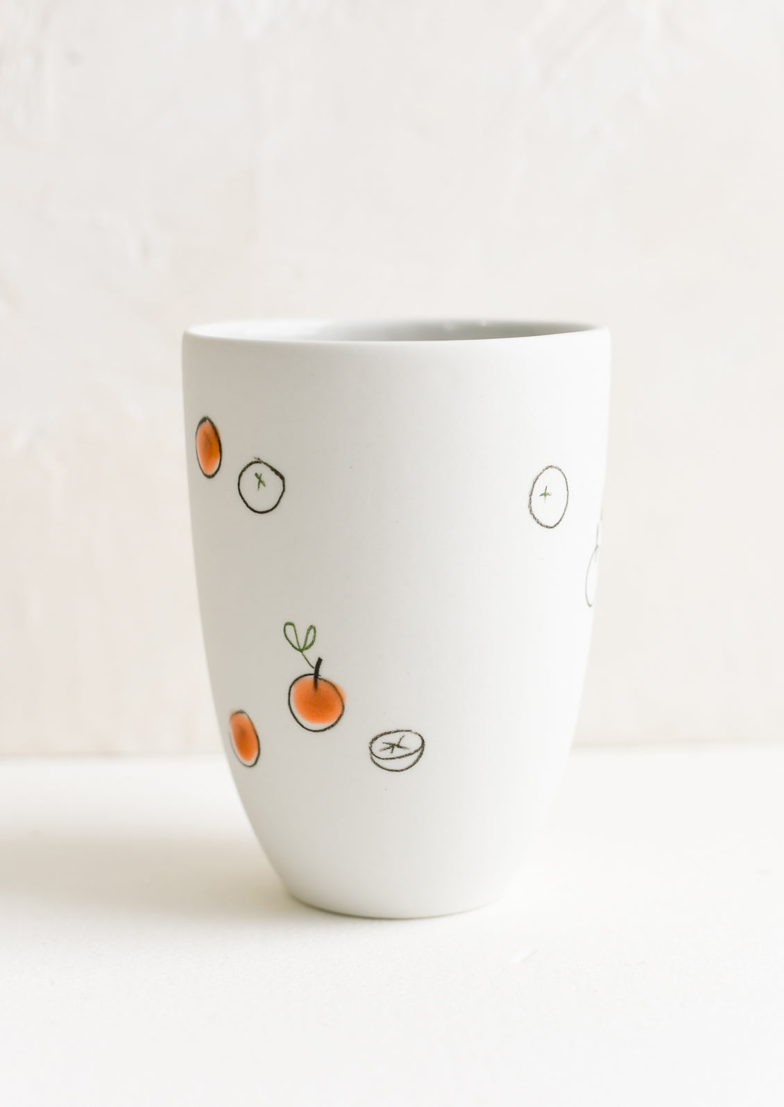 A tall porcelain cup with hand drawn oranges.