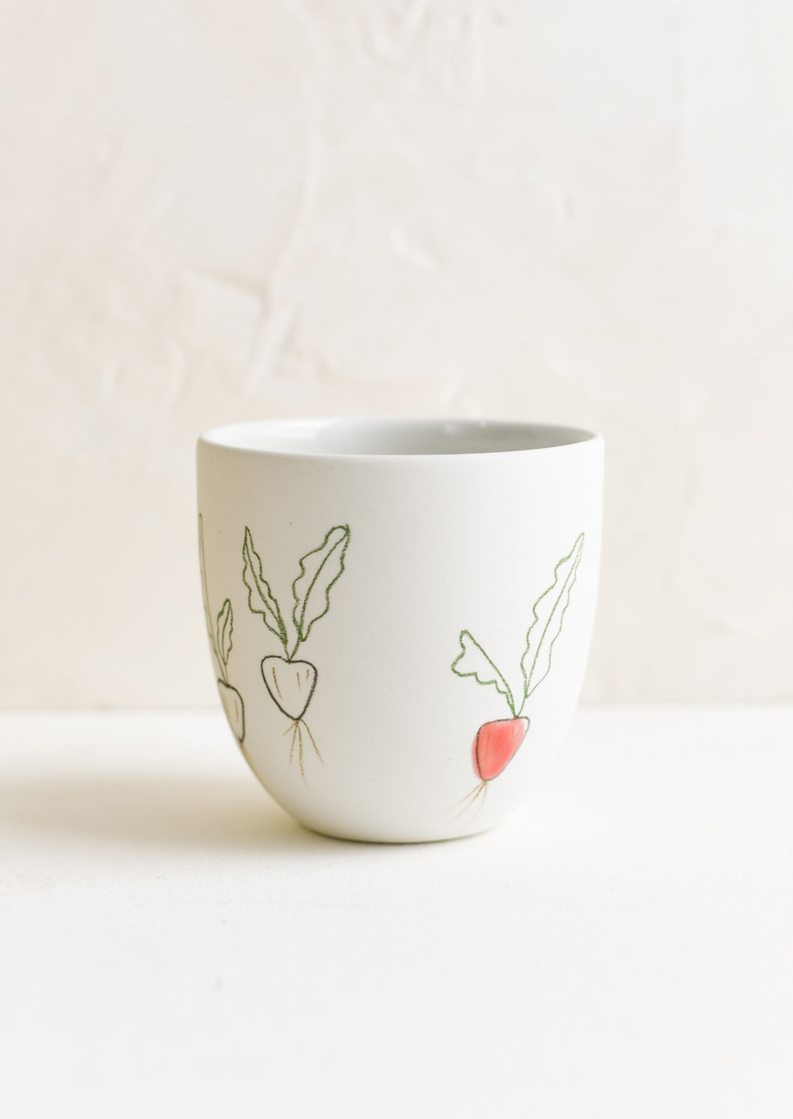 A small porcelain cup with hand drawn radishes.