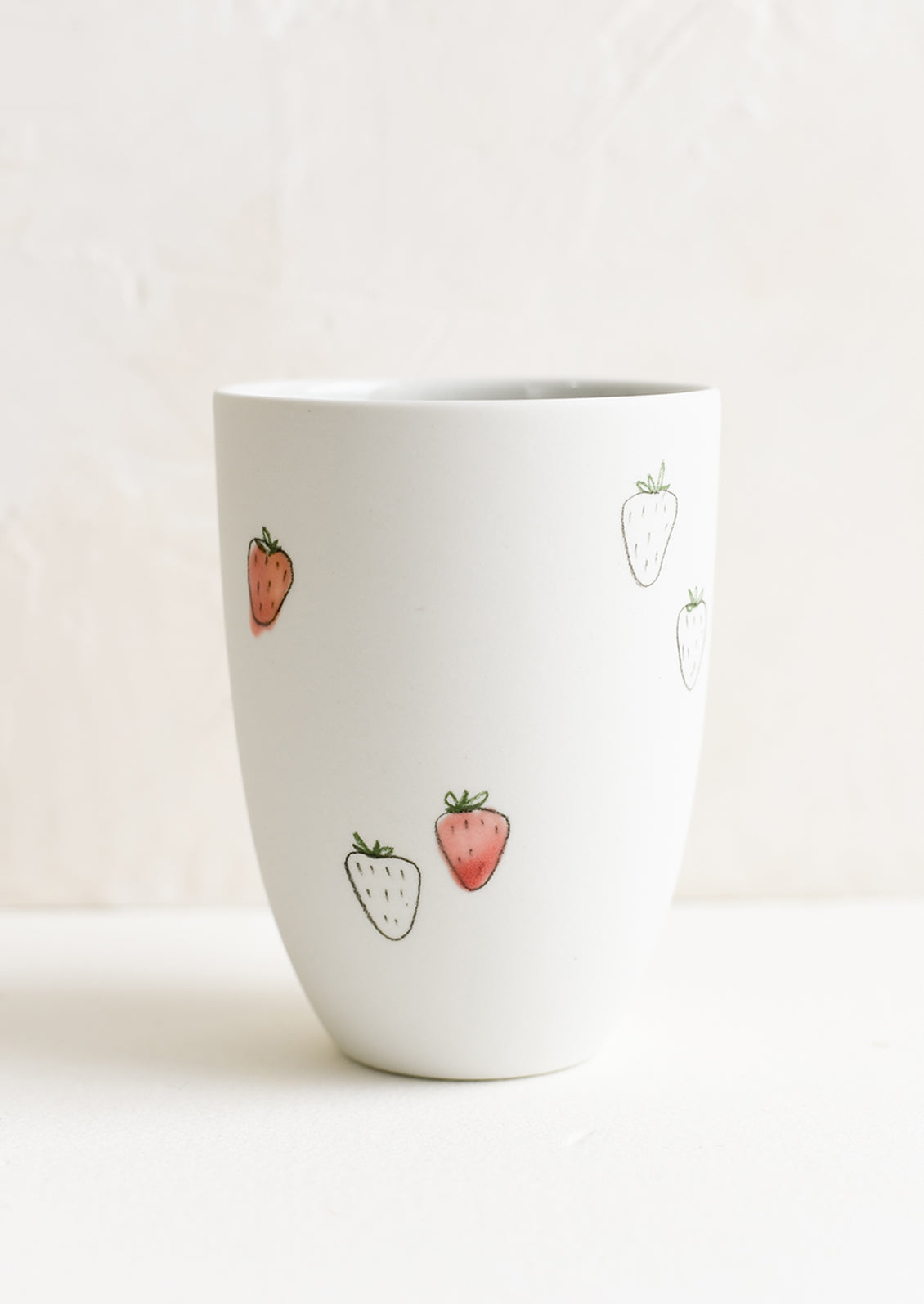 A tall porcelain cup with hand drawn strawberries.