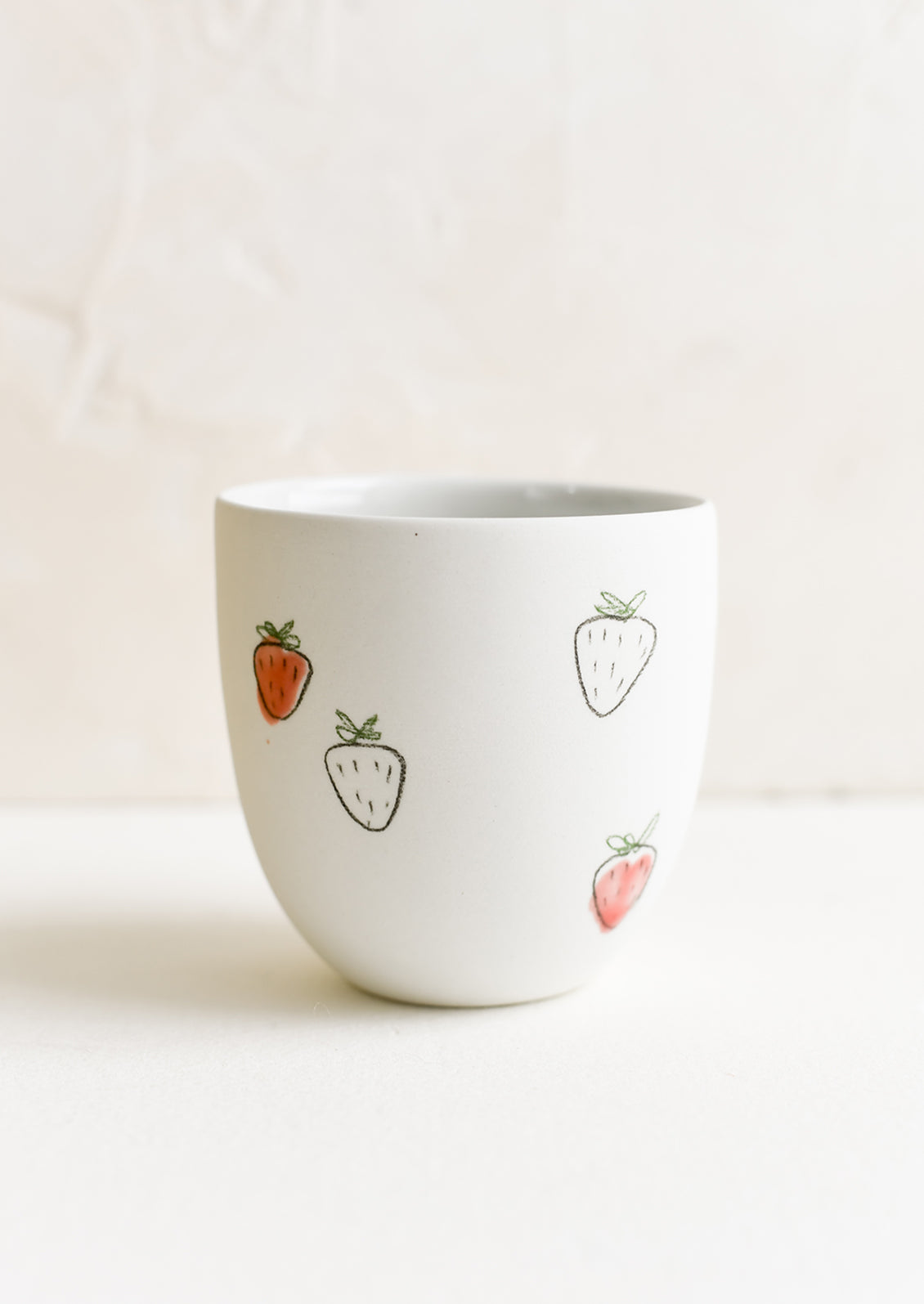 A small porcelain cup with hand drawn strawberries.