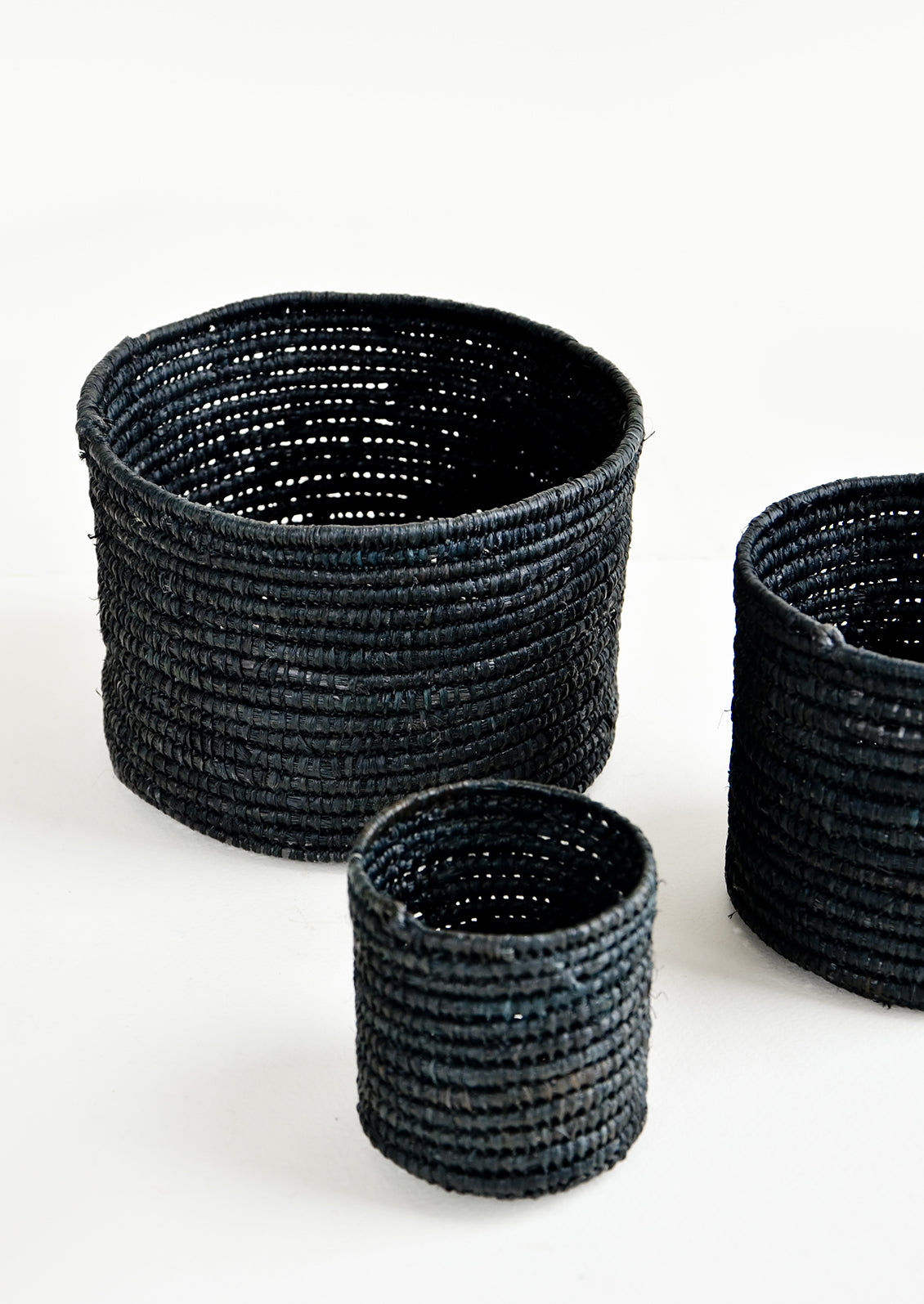 Set of round catchall baskets made black raffia in three incremental sizes.