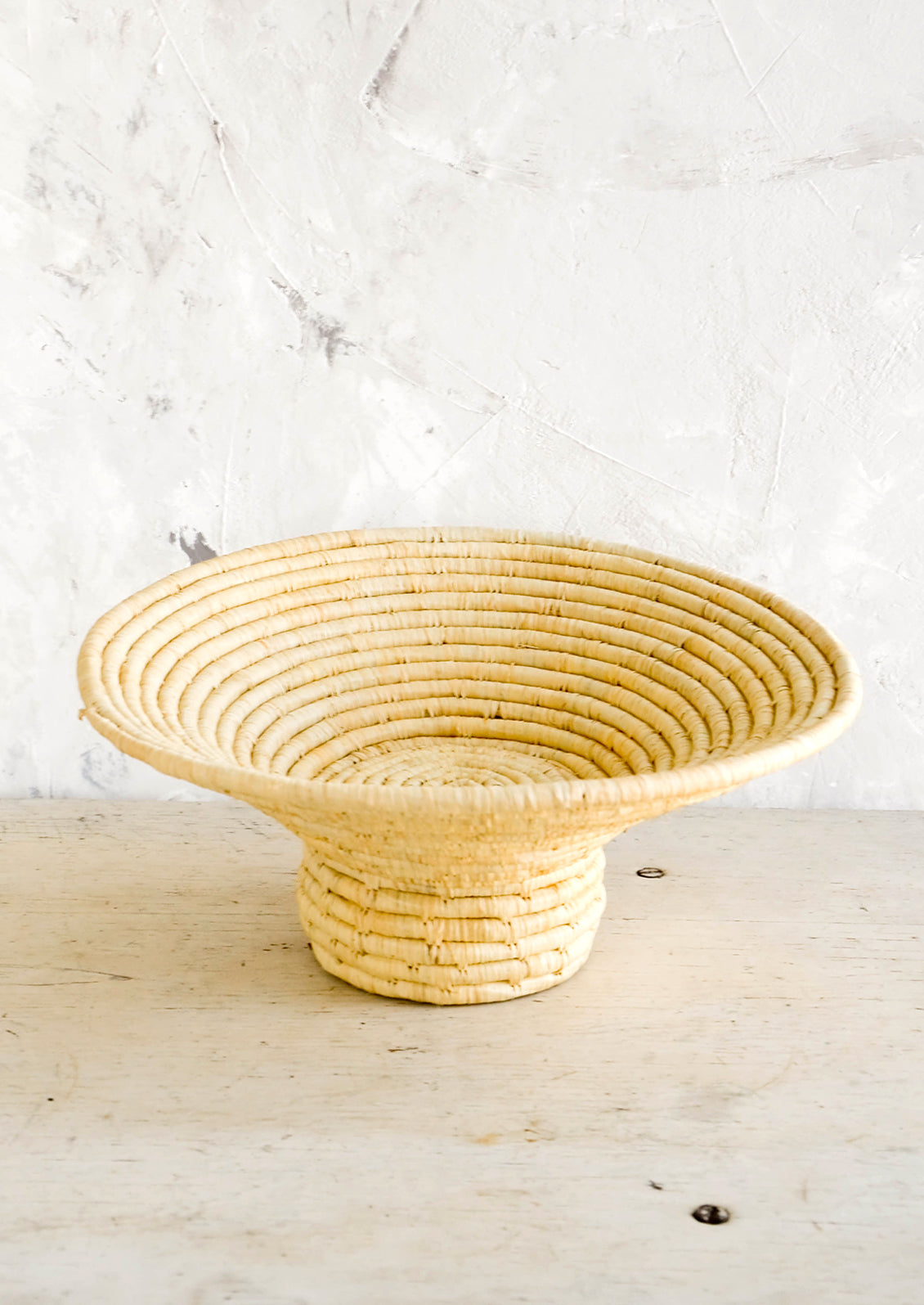 Footed pedestal bowl made from natural woven raffia, sitting on a table
