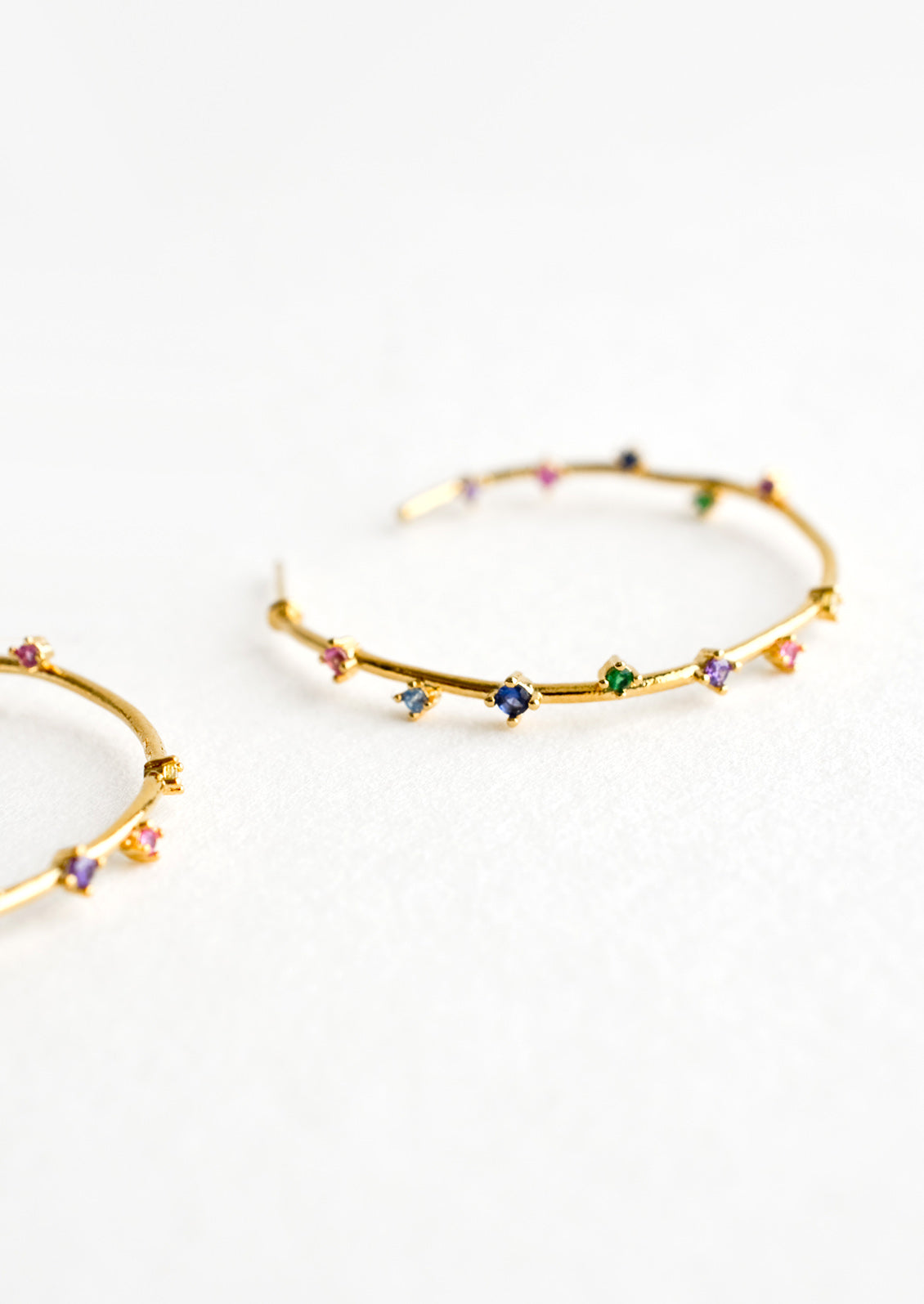 A pair of gold hoop earrings with colored crystals wrapping around the hoop sporadically.