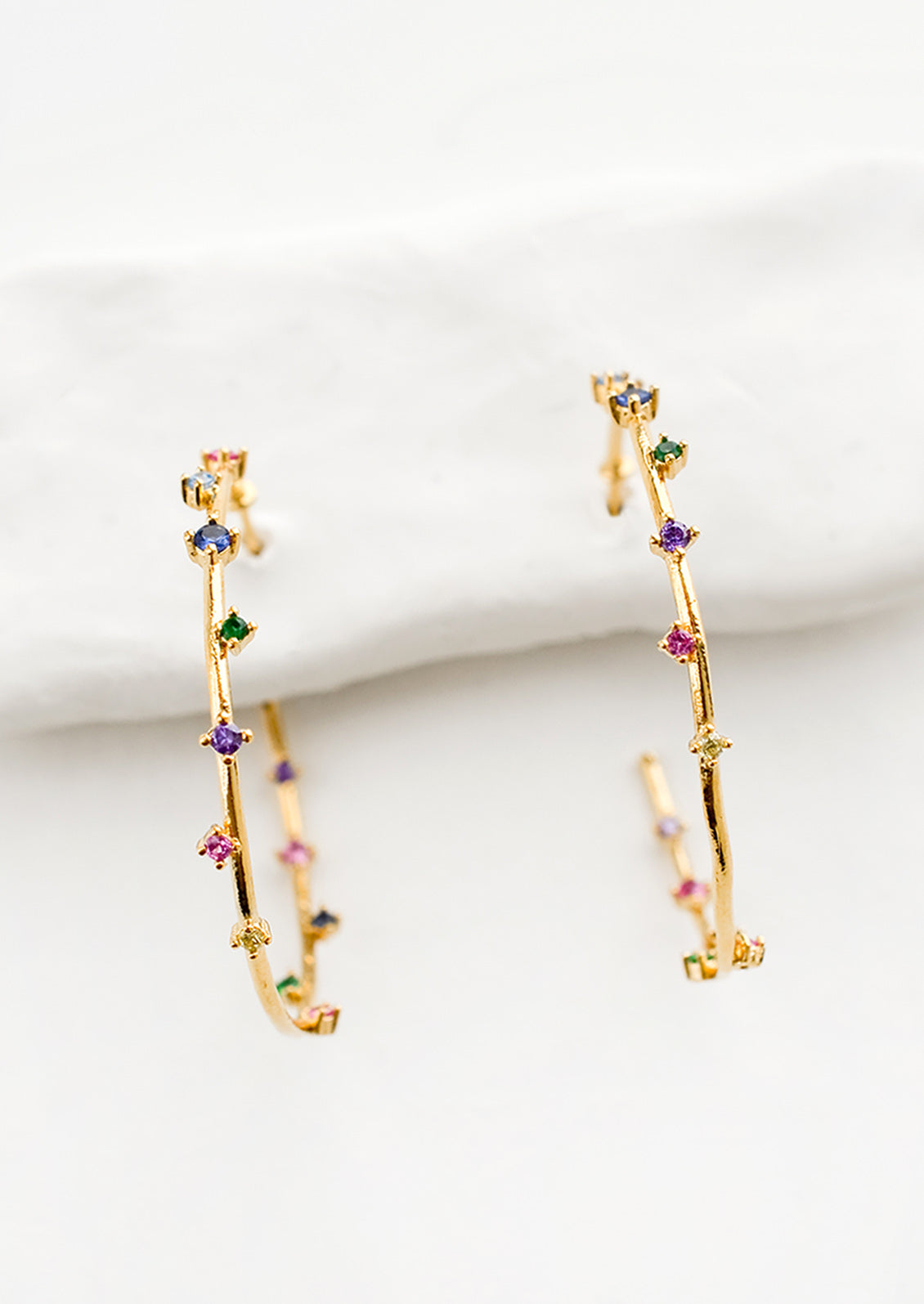 A pair of gold hoop earrings with colored crystals wrapping around the hoop sporadically.
