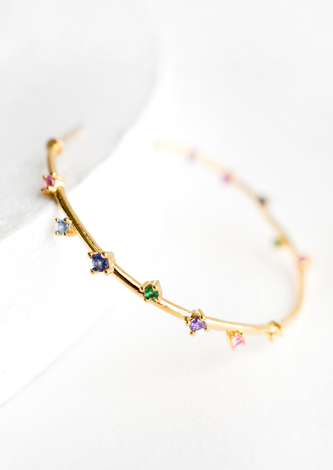 A gold hoop earring with colored crystal detailing.