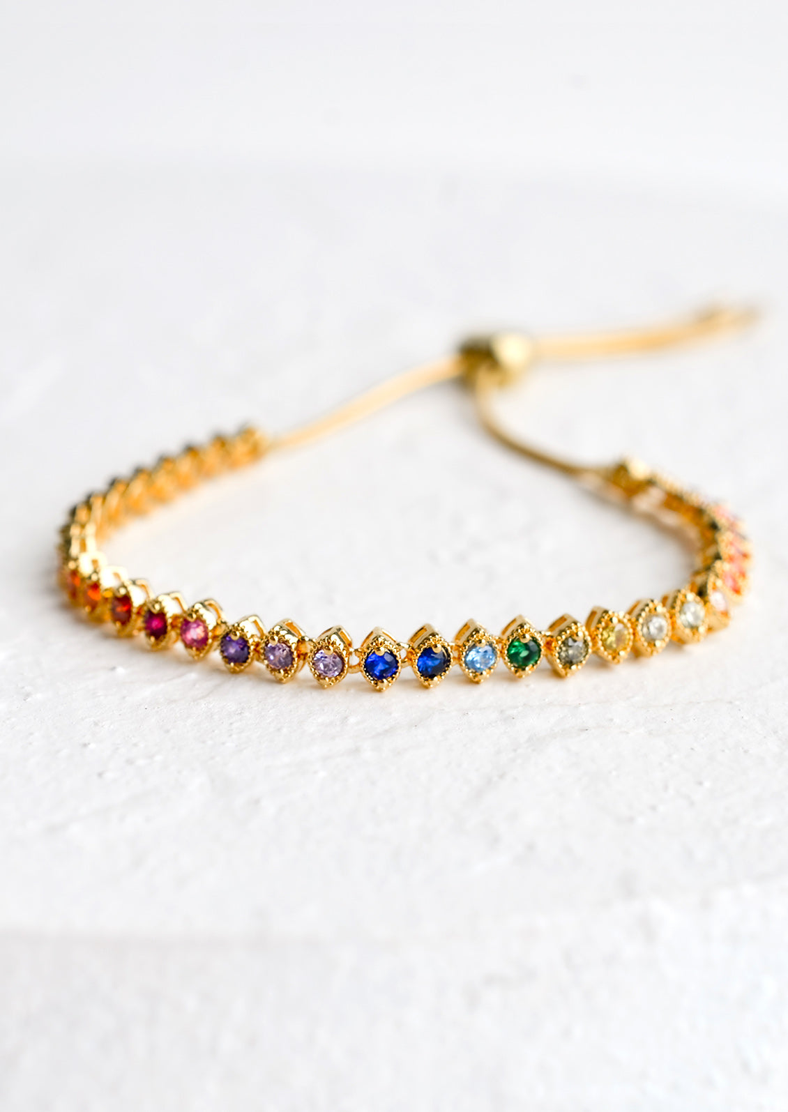 A gold, tennis style bracelet with marquis shaped crystals in rainbow color span.