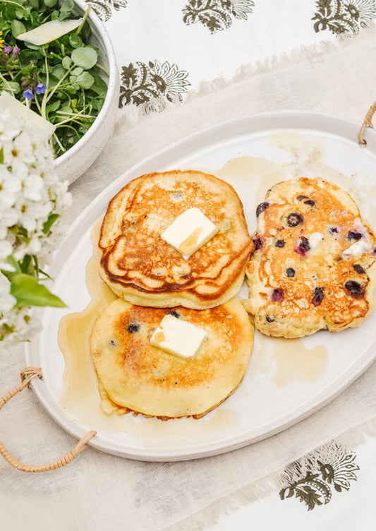 A breakfast table setting with pancakes on a ceramic serving platter.