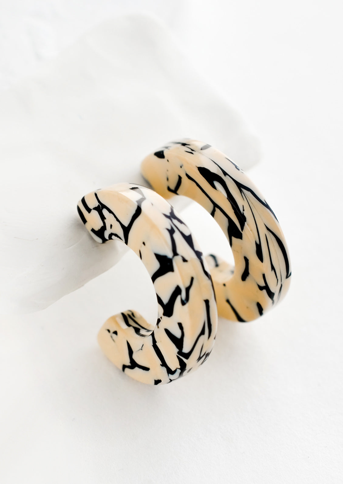 A pair of acetate hoop earrings in tan and black.