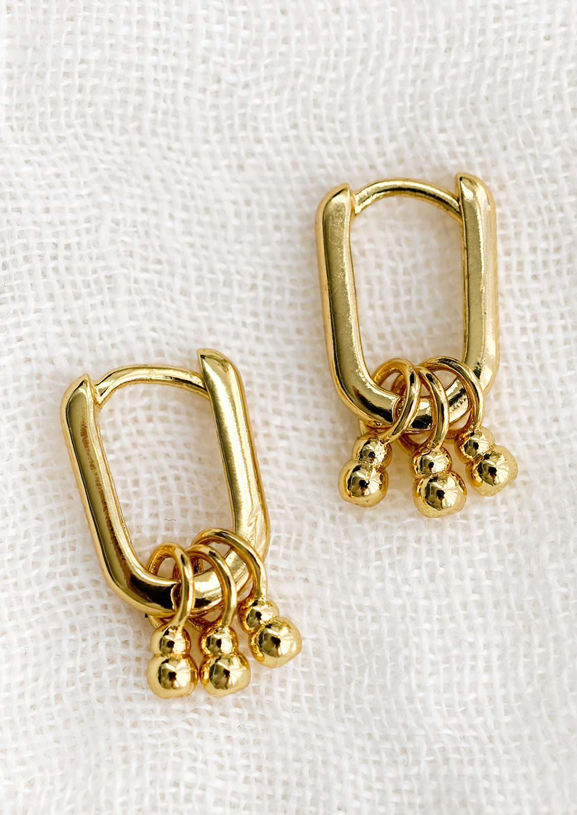 A pair of oval shape gold earrings with three beaded charm details.