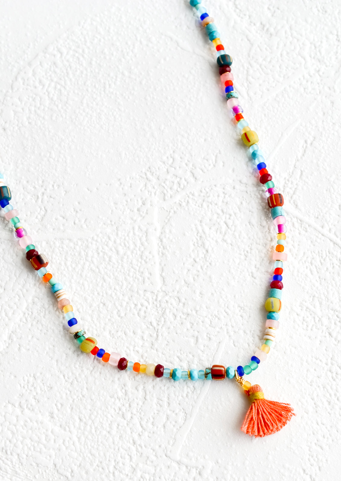 Colorful beaded necklace with peach tassel at center.