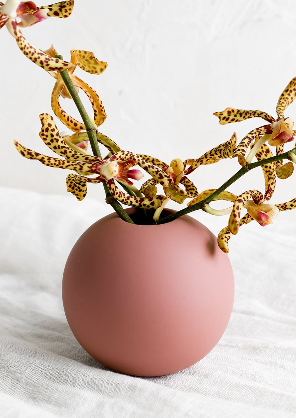 A round matte vase in dusty rose color, with tiger lilies.