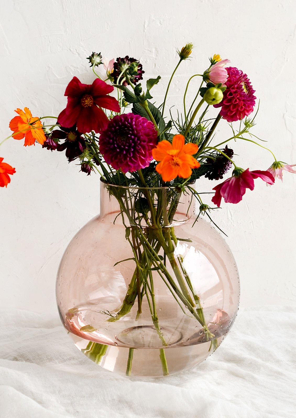 A round shaped glass vase in transparent pink, holding fresh flowers.
